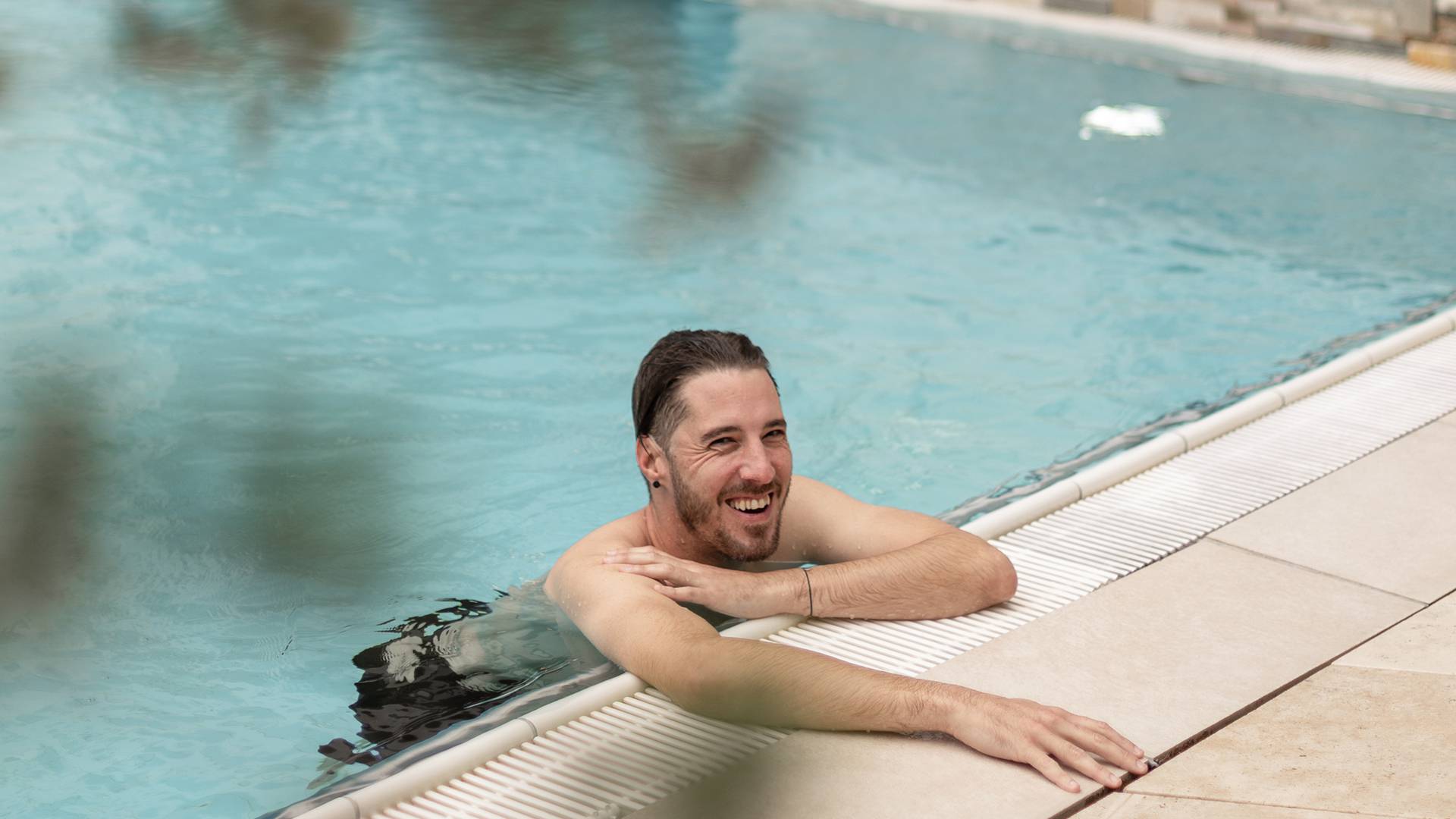 Mann im Pool hält sich am Beckenrand 